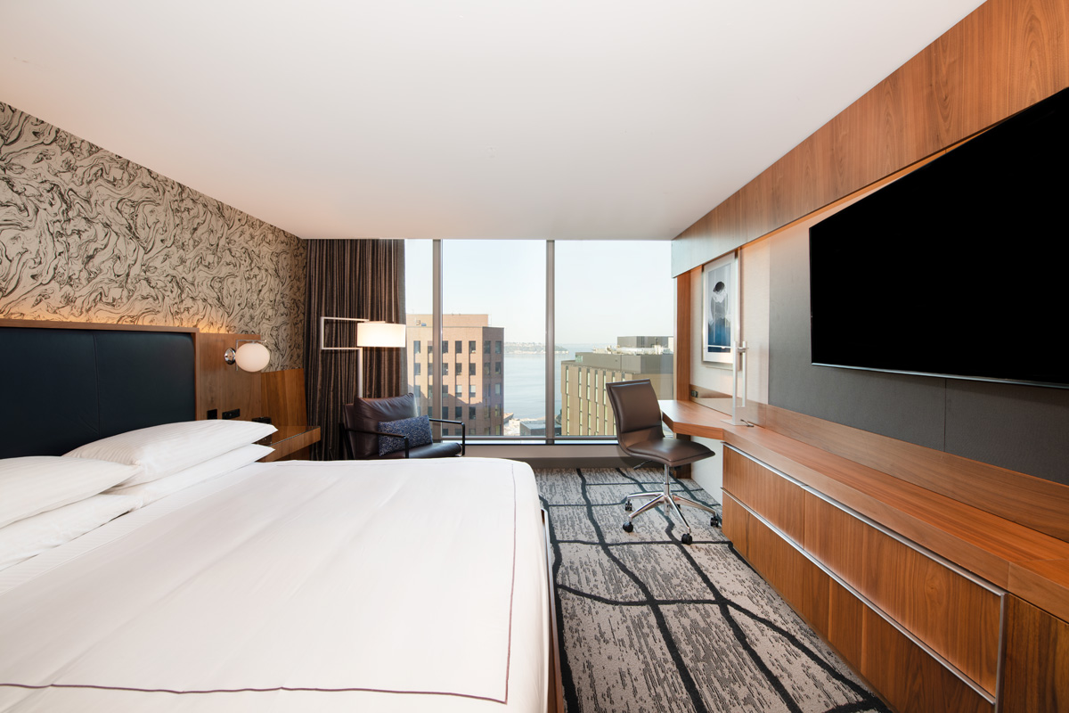 A hotel room with a large bed, TV, desk, and window with city view.